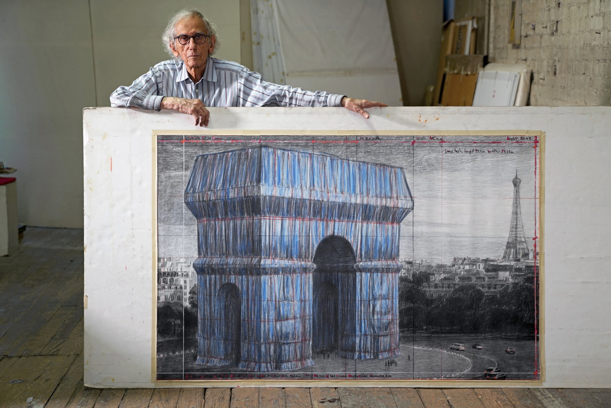 Christo in his studio with a preparatory drawing for L’Arc de Triomphe, Wrapped. Wolfgang Volz © 2019 Christo and Jeanne-Claude Foundation title=